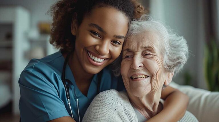 An elderly woman and her adult daughter sit together holding hands in a warmly furnished room.